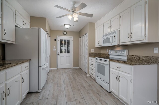 kitchen featuring ceiling fan, dark stone countertops, white appliances, white cabinets, and light wood-type flooring