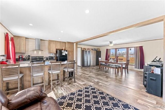 kitchen featuring light wood-style floors, wall chimney exhaust hood, a kitchen breakfast bar, black appliances, and recessed lighting