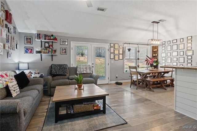 living room with lofted ceiling, french doors, wood-type flooring, and a textured ceiling