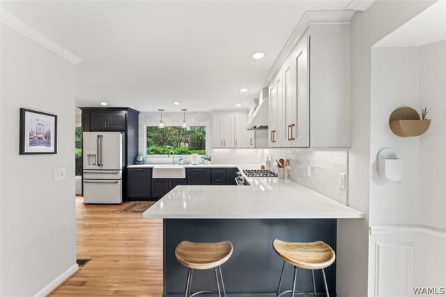 kitchen with sink, a kitchen breakfast bar, light hardwood / wood-style flooring, white refrigerator with ice dispenser, and kitchen peninsula