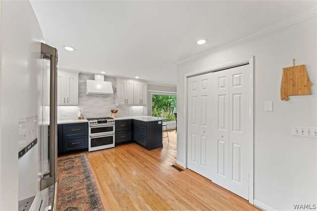 kitchen with premium range hood, crown molding, double oven range, white cabinets, and light hardwood / wood-style floors