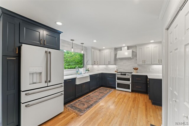 kitchen featuring custom exhaust hood, sink, pendant lighting, high quality appliances, and light hardwood / wood-style floors