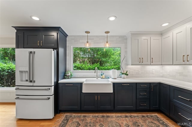 kitchen featuring pendant lighting, white refrigerator with ice dispenser, sink, hardwood / wood-style flooring, and tasteful backsplash