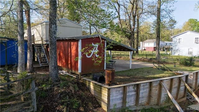 view of outdoor structure with an outdoor structure, an attached carport, fence, and stairs