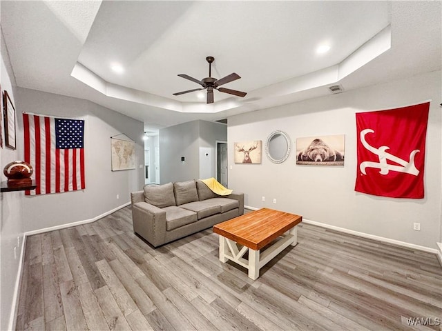 living area featuring baseboards, a tray ceiling, and wood finished floors