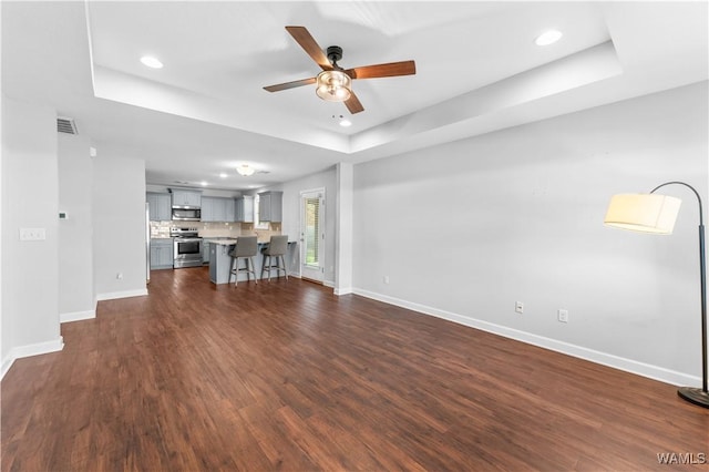 unfurnished living room featuring a tray ceiling, recessed lighting, dark wood finished floors, and baseboards