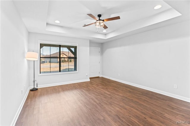 empty room with dark wood-style floors, baseboards, a tray ceiling, and ceiling fan