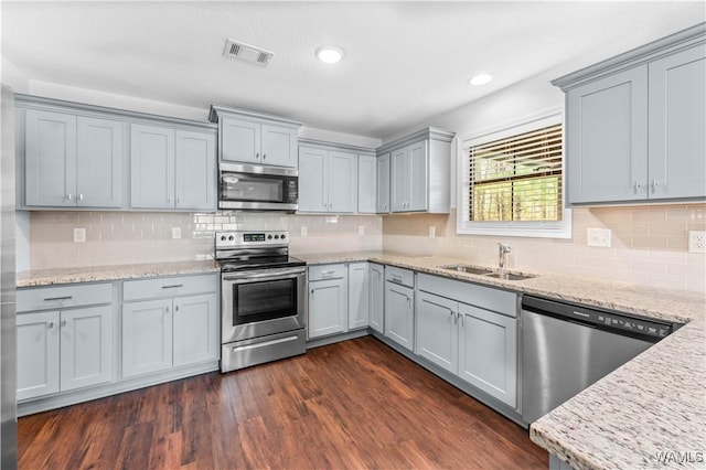 kitchen with stainless steel appliances, visible vents, dark wood-type flooring, a sink, and light stone countertops