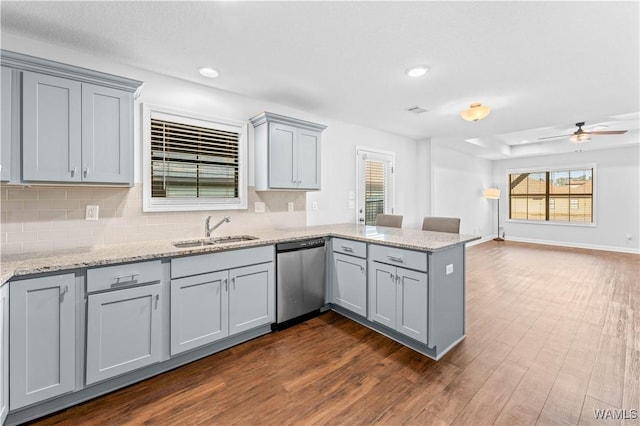 kitchen featuring gray cabinetry, a peninsula, a sink, dishwasher, and dark wood finished floors