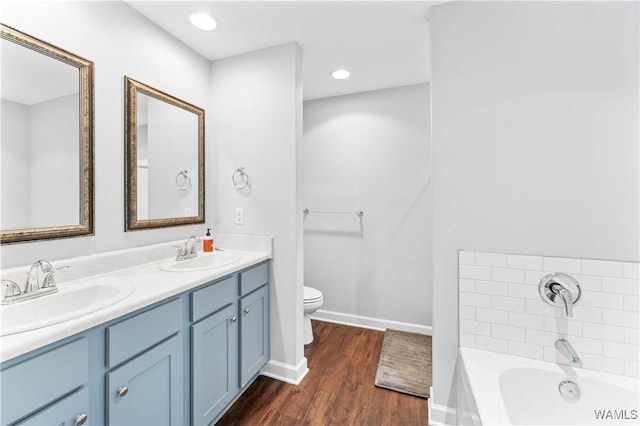 bathroom featuring a garden tub, a sink, toilet, and wood finished floors