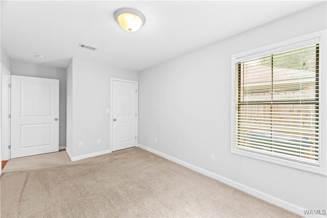 unfurnished bedroom featuring carpet floors, baseboards, multiple windows, and visible vents