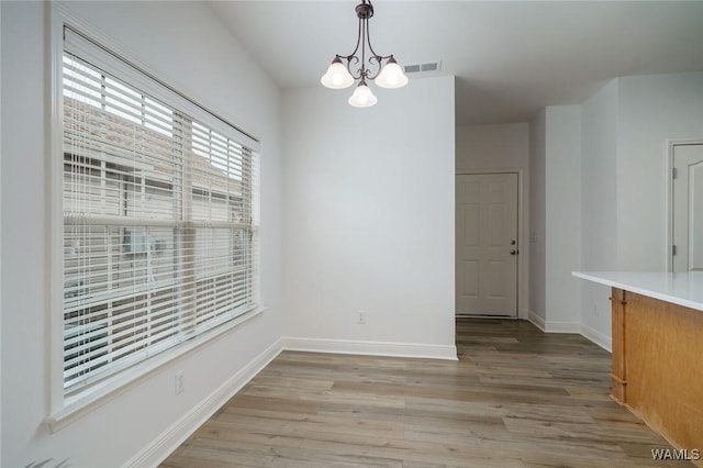 unfurnished dining area with a notable chandelier and light hardwood / wood-style flooring