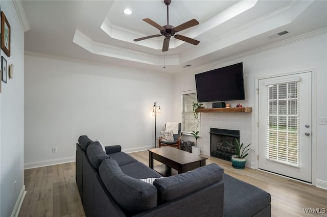 living room with hardwood / wood-style floors, a tray ceiling, a fireplace, and ornamental molding