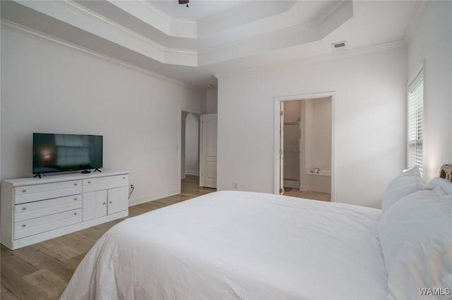 bedroom featuring crown molding, connected bathroom, a tray ceiling, and light hardwood / wood-style floors