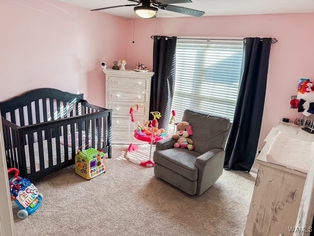 carpeted bedroom with ceiling fan and a nursery area