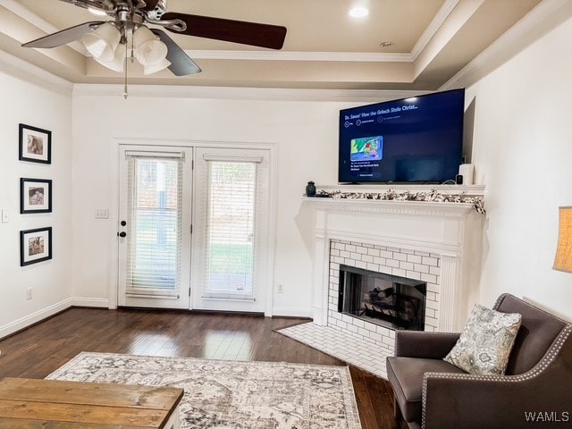 living room with a raised ceiling, a fireplace, crown molding, and dark hardwood / wood-style flooring