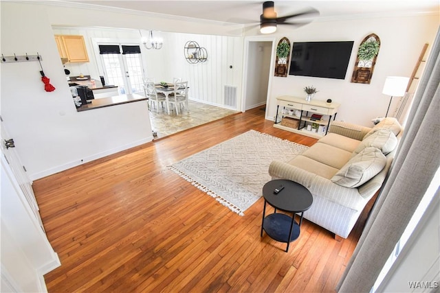 living room with wood finished floors, visible vents, baseboards, crown molding, and ceiling fan with notable chandelier