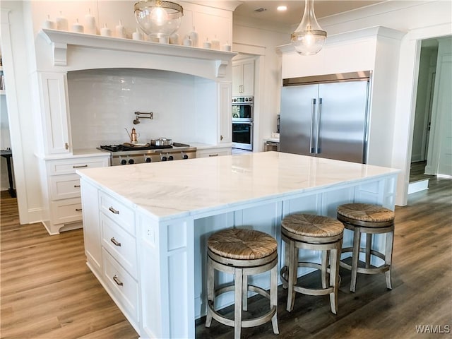 kitchen with white cabinets, stainless steel appliances, a kitchen island, and hardwood / wood-style floors