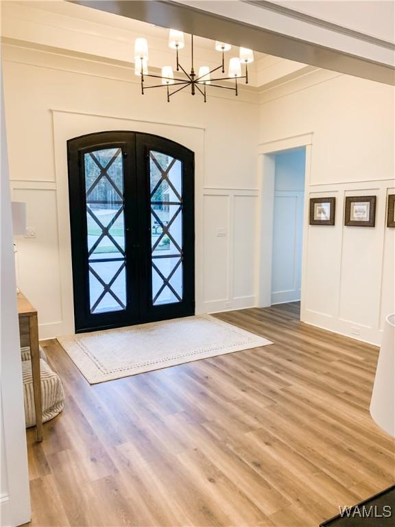 foyer featuring french doors, light hardwood / wood-style flooring, ornamental molding, and a chandelier