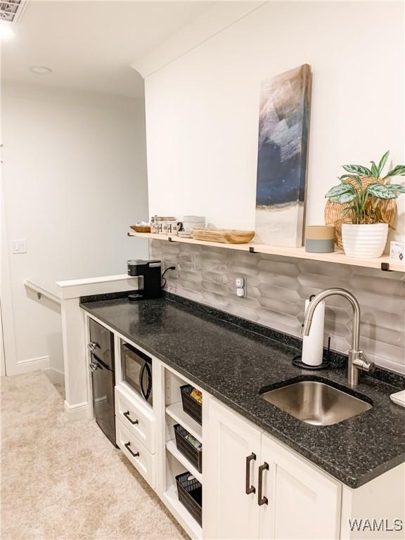 kitchen with tasteful backsplash, light carpet, white cabinets, dark stone countertops, and sink