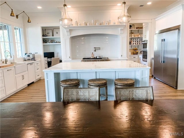 kitchen with white cabinetry, hanging light fixtures, sink, stainless steel built in refrigerator, and a breakfast bar area