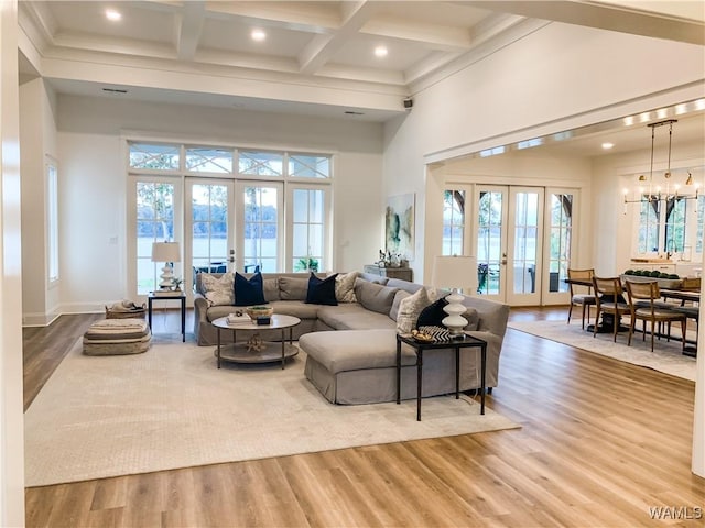 living room with french doors, hardwood / wood-style flooring, a towering ceiling, a notable chandelier, and beamed ceiling