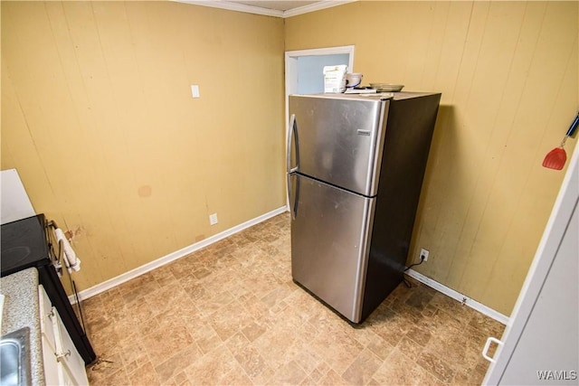 kitchen featuring wooden walls, white cabinetry, stainless steel fridge, ornamental molding, and range