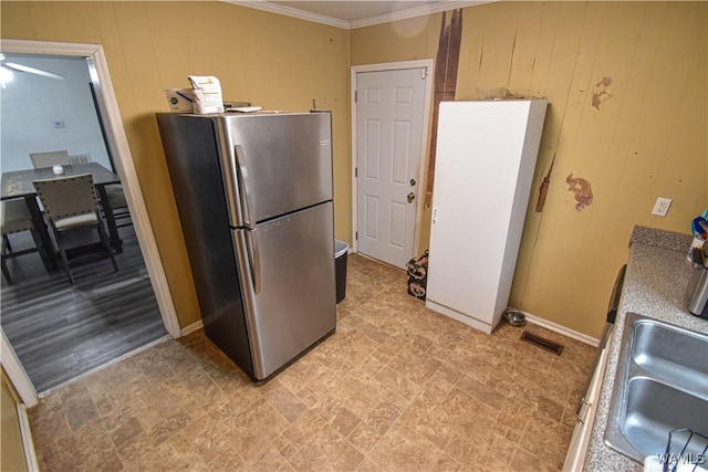 kitchen with crown molding, white fridge, wooden walls, and stainless steel refrigerator