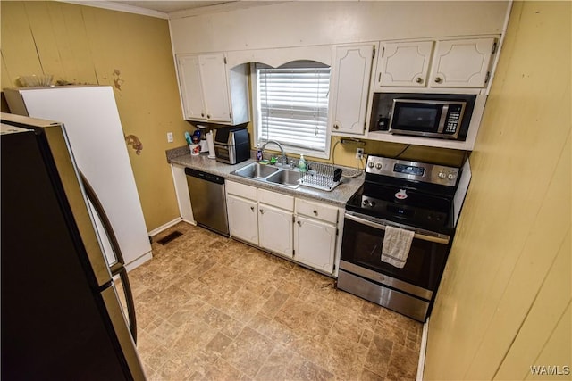 kitchen with sink, appliances with stainless steel finishes, white cabinetry, wooden walls, and ornamental molding