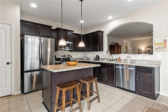 kitchen with appliances with stainless steel finishes, decorative light fixtures, decorative backsplash, a center island, and light tile patterned floors