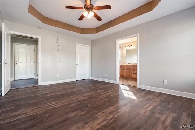 unfurnished bedroom with a raised ceiling, ceiling fan, dark hardwood / wood-style flooring, and ensuite bath