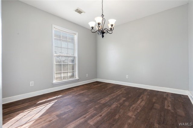 empty room featuring a wealth of natural light, dark hardwood / wood-style flooring, and a notable chandelier