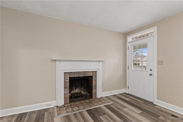 unfurnished living room with a tiled fireplace and dark hardwood / wood-style flooring