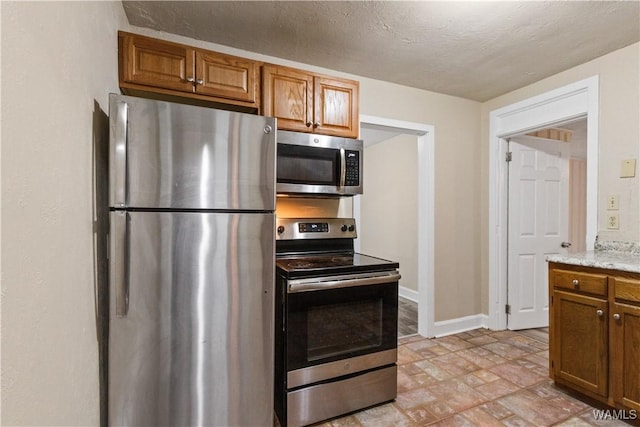 kitchen with stainless steel appliances, a textured ceiling, and light stone counters