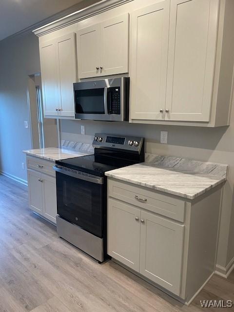 kitchen with stainless steel appliances, white cabinets, light stone counters, and light hardwood / wood-style flooring