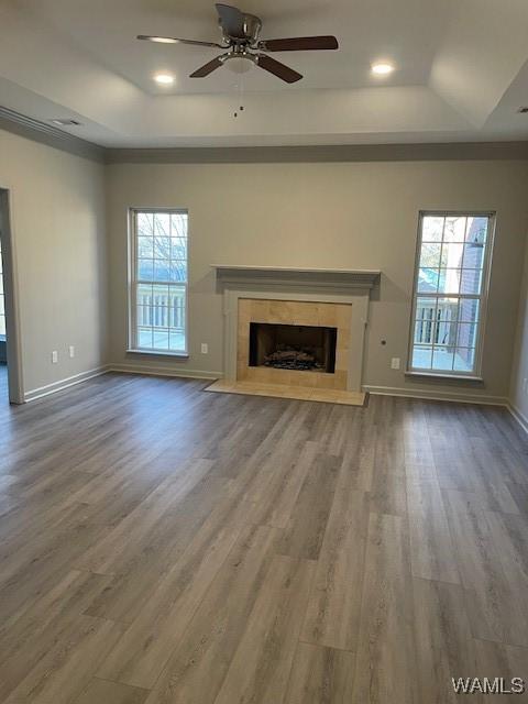 unfurnished living room featuring a raised ceiling, a tile fireplace, hardwood / wood-style flooring, and ceiling fan