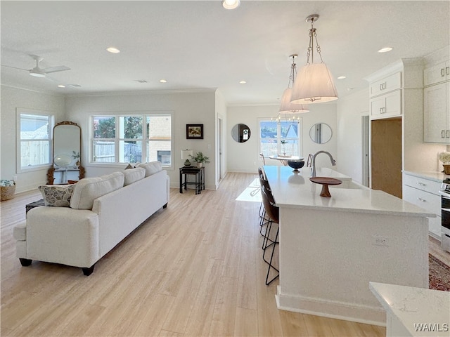 kitchen with sink, an island with sink, light hardwood / wood-style floors, and decorative light fixtures