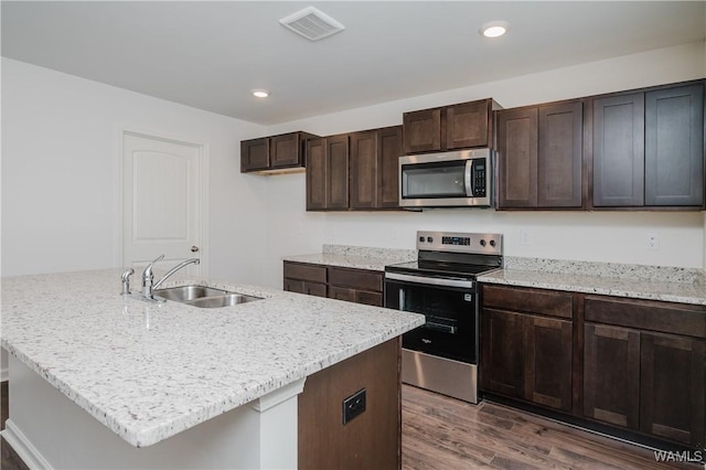 kitchen featuring a center island with sink, dark wood-type flooring, stainless steel appliances, dark brown cabinetry, and sink