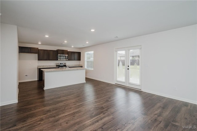 kitchen with a center island with sink, dark brown cabinets, stainless steel appliances, and dark wood-type flooring