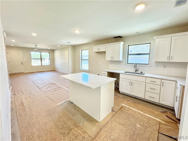 kitchen with sink, a center island, light stone counters, white cabinets, and decorative backsplash