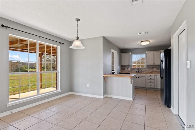 kitchen featuring visible vents, decorative backsplash, a peninsula, freestanding refrigerator, and light tile patterned flooring