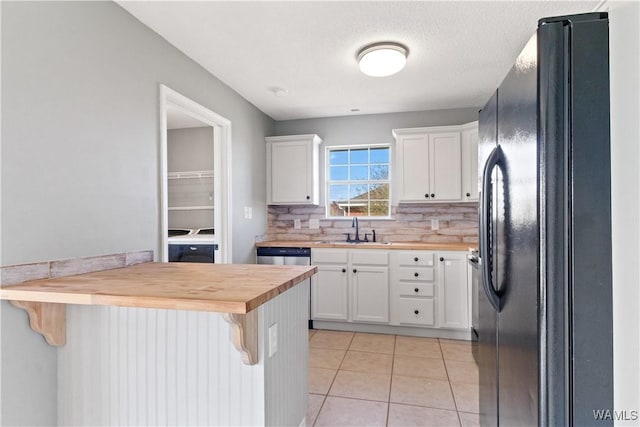 kitchen featuring a kitchen bar, a sink, freestanding refrigerator, light tile patterned floors, and wooden counters