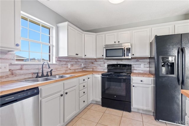 kitchen with light tile patterned flooring, a sink, black appliances, white cabinets, and backsplash