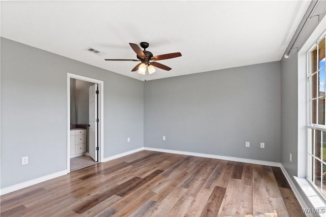 unfurnished bedroom featuring visible vents, ceiling fan, baseboards, ensuite bathroom, and wood finished floors