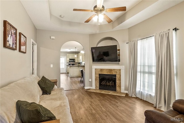 4458 19th St, Northport, AL 35476 - living room with wood finished floors, a tray ceiling, a ceiling fan, a tiled fireplace, and arched walkways