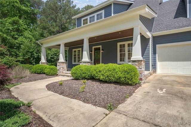 entrance to property with a garage, covered porch, stone siding, a shingled roof, and concrete driveway