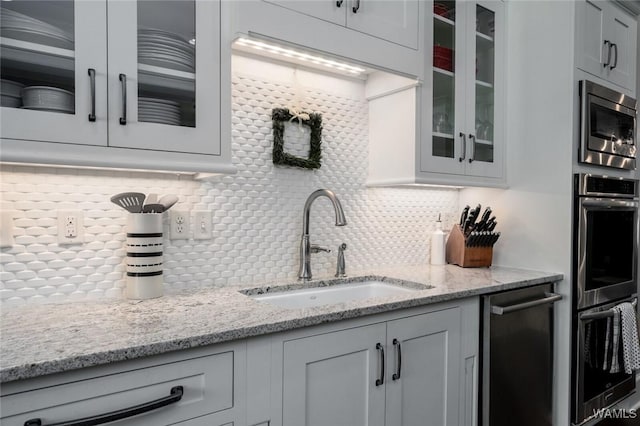 kitchen with light stone countertops, appliances with stainless steel finishes, backsplash, and sink