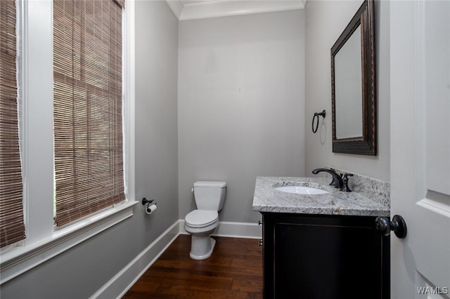 half bath featuring vanity, baseboards, wood finished floors, and toilet