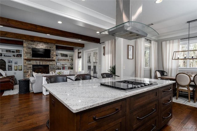 kitchen featuring a stone fireplace, built in features, light stone counters, island exhaust hood, and stainless steel gas cooktop