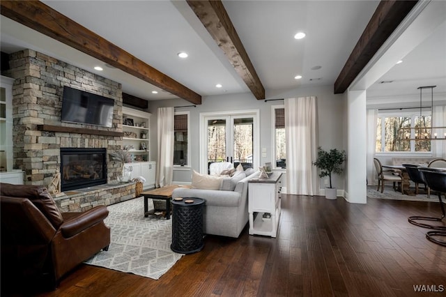 living room featuring beam ceiling, a stone fireplace, plenty of natural light, and dark wood-type flooring